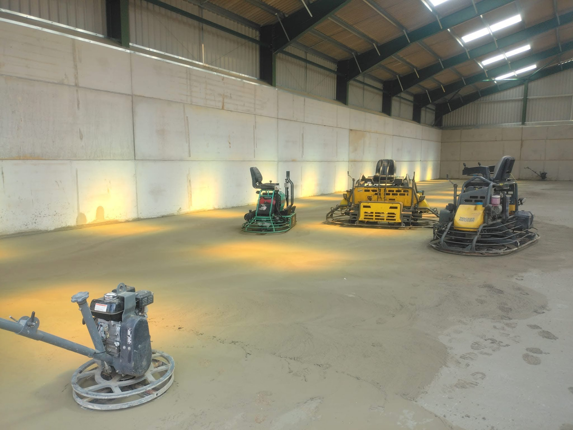 Power-float machines finishing a concrete floor inside a steel-framed building