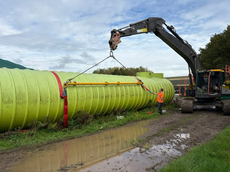 Excavator positioning a large tank during groundworks